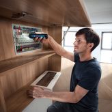 一个人使用无绳螺丝刀固定配电盘中的电线。.