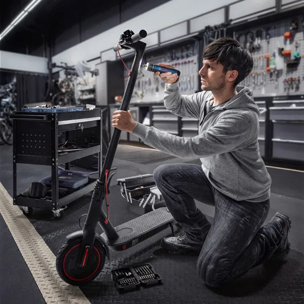 一个人跪下来，用无绳螺丝刀修理电动滑板车。.