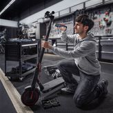 一个人跪下来，用无绳螺丝刀修理电动滑板车。.