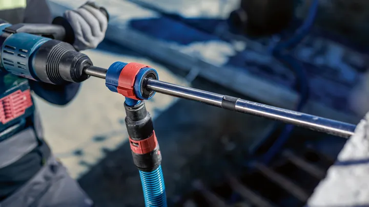 一名佩戴安全设备的人员使用旋转工具在混凝土中钻孔。