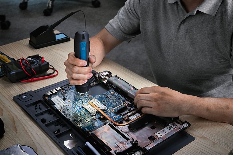 一个人在工作台上使用无绳螺丝刀组装笔记本电脑。.