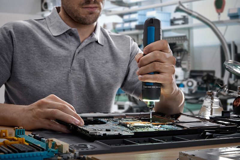 人员使用无绳螺丝刀组装电路板上的电子元件。.