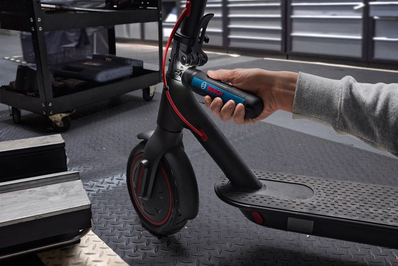 一个人用无绳螺丝刀调整电动滑板车的车把。.