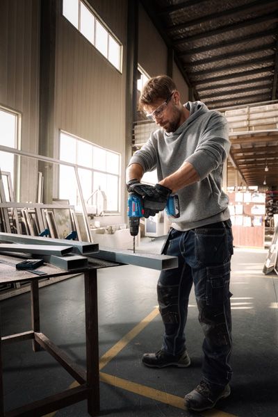 一名佩戴安全设备的人员在车间内钻入金属梁。.