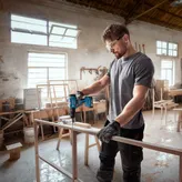 一名佩戴安全设备的人员在车间内钻入木制框架。.