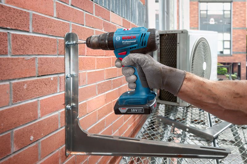 一名佩戴安全设备的人员使用无绳电钻将金属支架固定在砖墙上。.