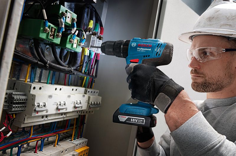 一名佩戴安全设备的人正在钻进布满电线的控制面板。.