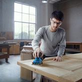 一名佩戴安全设备的人员正在用手持式电动砂光机打磨木门。.