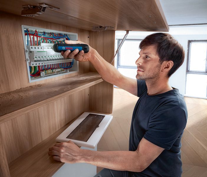 一个人使用无绳螺丝刀来紧固电气面板上的元件。.