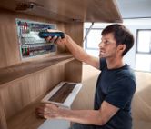 一个人使用无绳螺丝刀来紧固电气面板上的元件。.