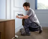 一个人使用无绳螺丝刀安装电源插座盖。.