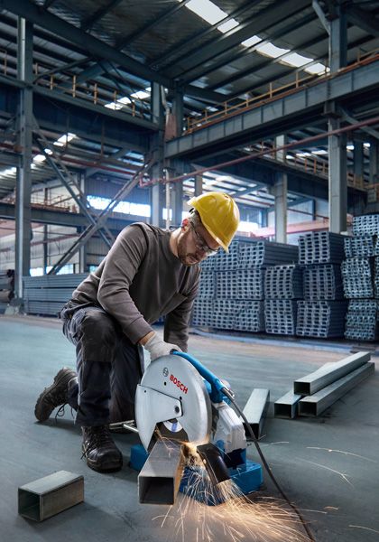 一名佩戴安全设备的人员在仓库里用切割锯切割金属管。.