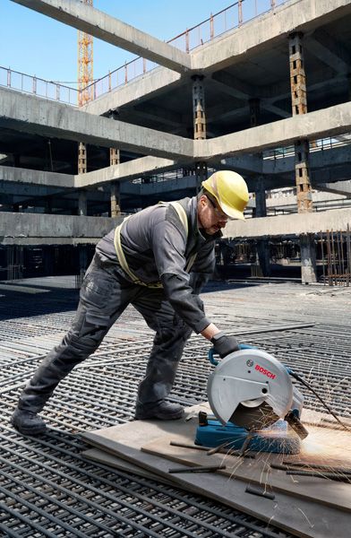 一名佩戴安全设备的人员在建筑工地用切割锯切割金属管道。.