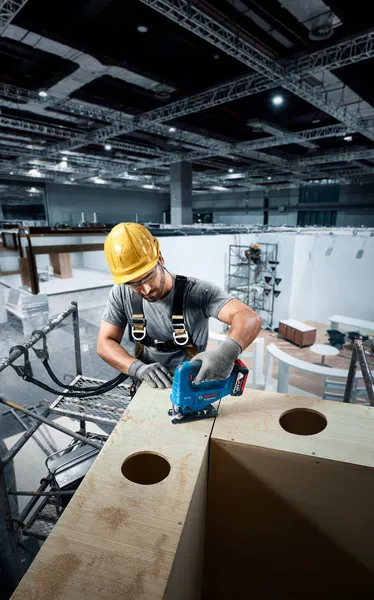 建筑工地上，一名佩戴安全设备的人员正在使用曲线锯切割木材。.