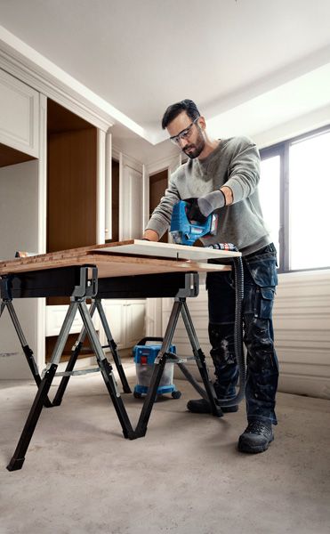 一名佩戴安全设备的人员在工作台上使用曲线锯切割木材。.