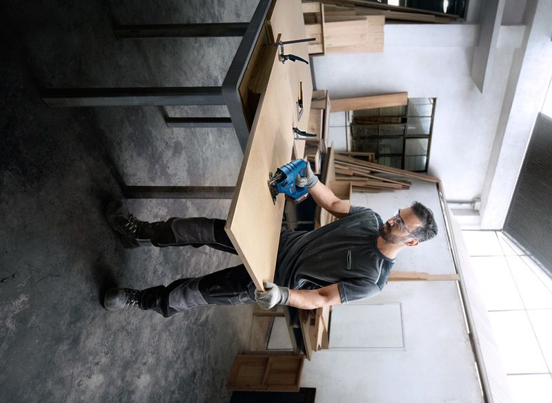 一名佩戴安全设备的人员在车间使用电动工具切割木材。.