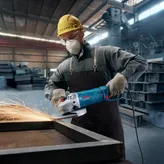 佩戴安全设备的人使用电动工具研磨金属，产生火花。.