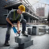 建筑工地上，一名佩戴安全设备的工人正在用电锯切割混凝土块。.