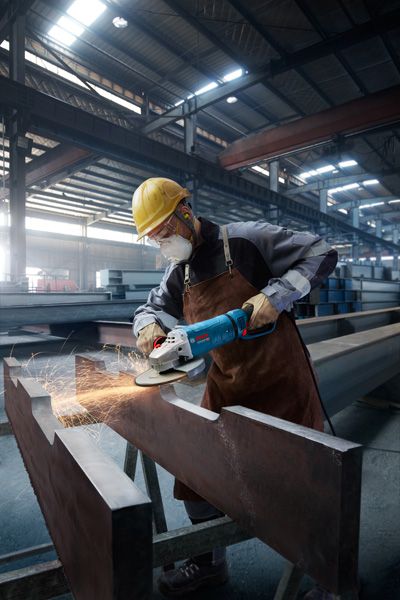 一名佩戴安全设备的人员正在用角磨机打磨一根大型金属梁。.