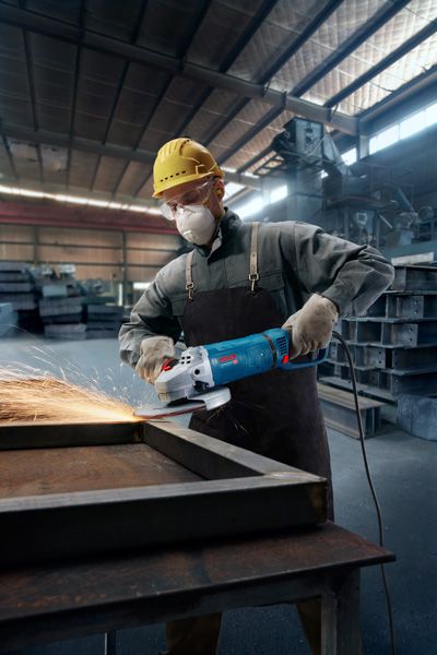 一名佩戴安全设备的工人在车间使用角磨机打磨金属框架。.