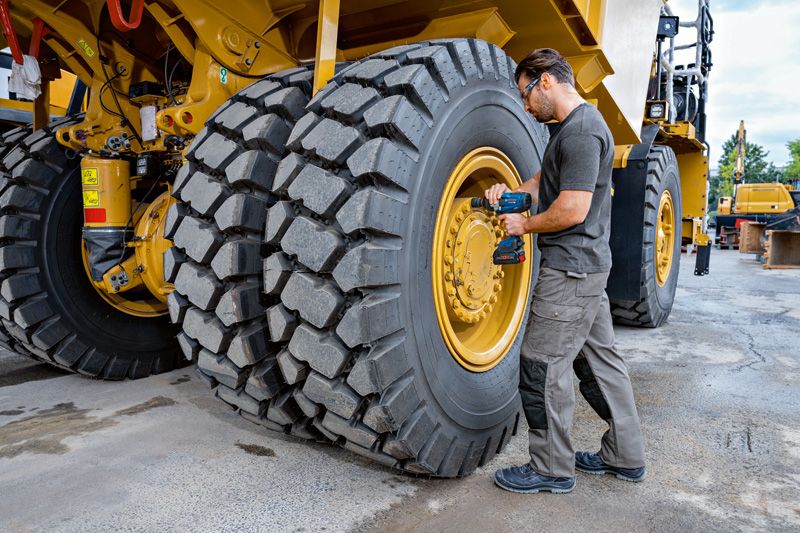 一名佩戴安全设备的人员使用冲击扳手拧紧大型工程车辆的轮胎。.