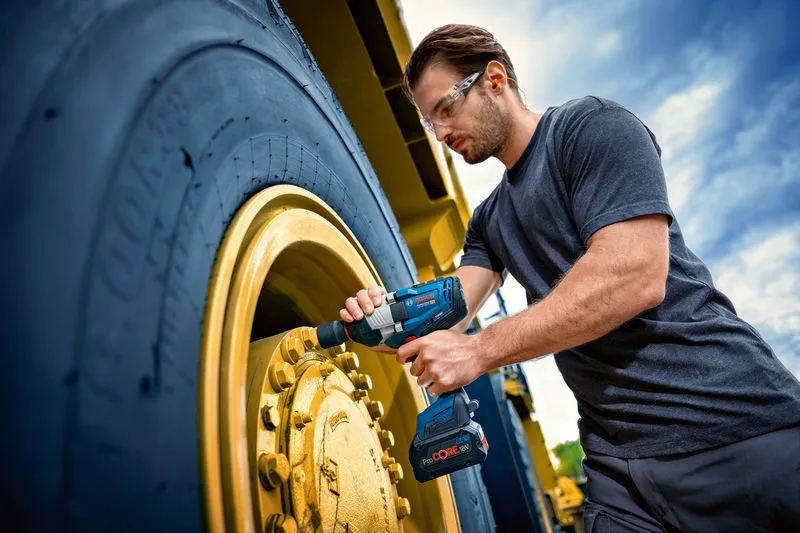 一名佩戴安全设备的人使用冲击扳手拧紧大型车轮。.