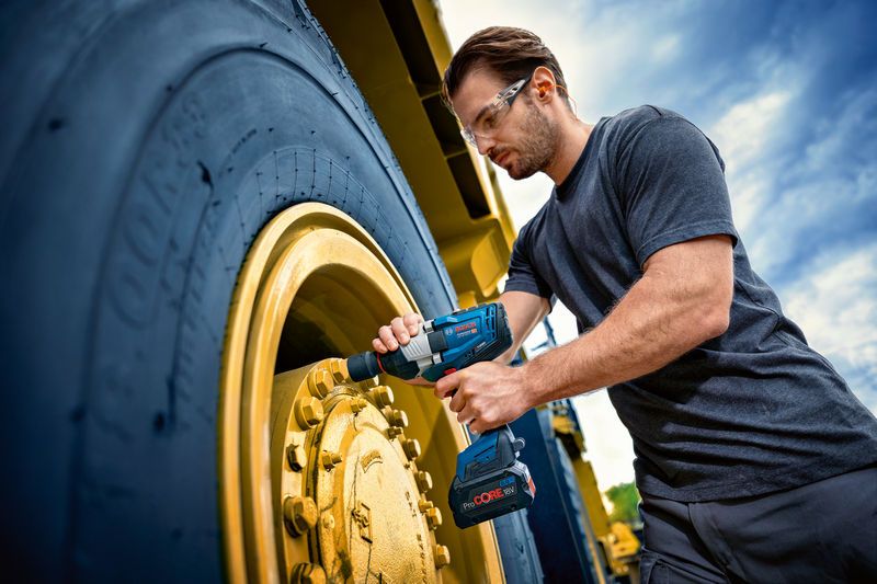 一名佩戴安全设备的人使用冲击扳手拧紧大型车轮。.