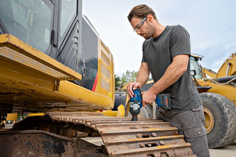 一名佩戴安全设备的人员在挖掘机履带上使用无绳冲击扳手。.