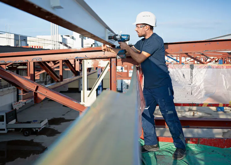 一名佩戴安全设备的人员使用无绳冲击扳手拧紧钢梁。.