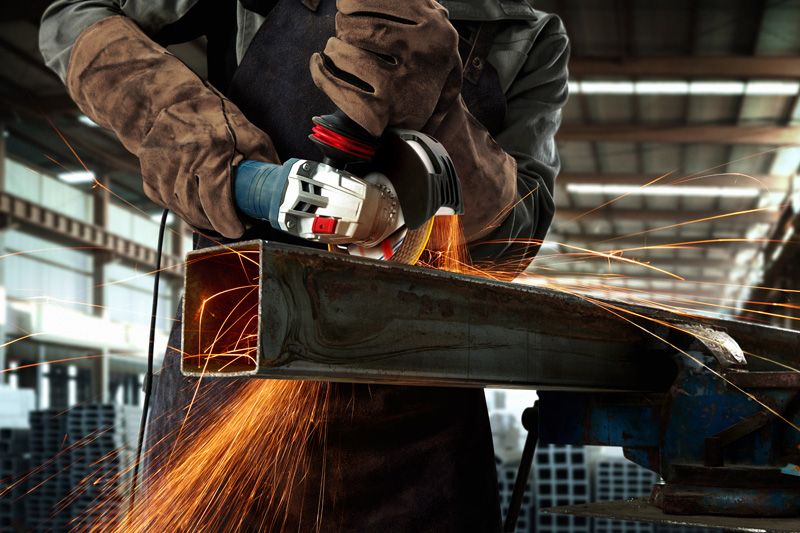 一名佩戴安全设备的人用角磨机打磨金属梁，产生火花。.