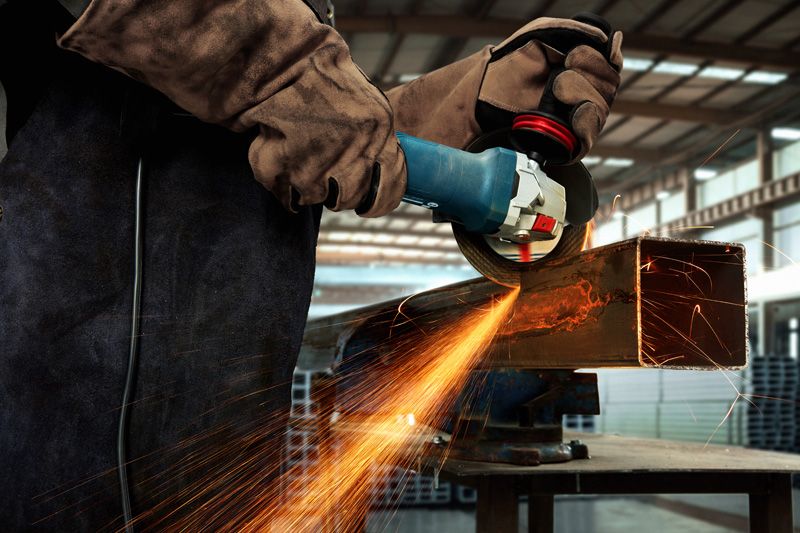 一名佩戴安全设备的人员正在使用角磨机打磨金属梁。.