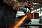 一名佩戴安全设备的人员正在使用角磨机打磨金属梁。.