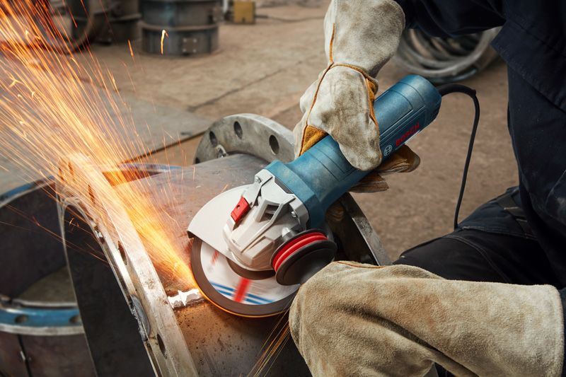 一名佩戴安全设备的人用角磨机打磨金属，产生火花。.