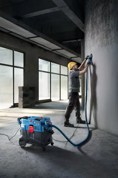 一名佩戴安全设备的人员使用多用途提取器打磨混凝土墙。.