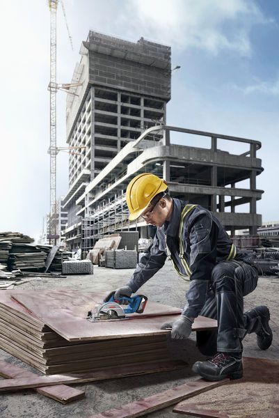一名佩戴安全设备的人员在建筑工地切割堆放的胶合板。.