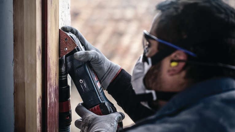 佩戴安全设备的人员使用电动工具打磨木制框架。