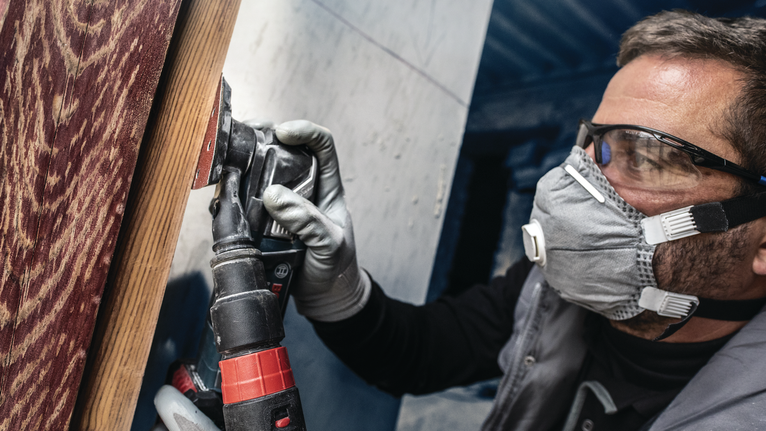 佩戴安全设备的人员使用电动工具打磨木质表面。