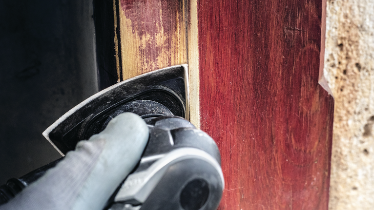 佩戴安全设备的人员使用电动工具打磨木门框。