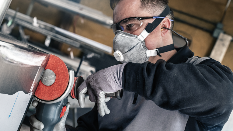 佩戴安全设备的人员使用电动工具抛光金属。