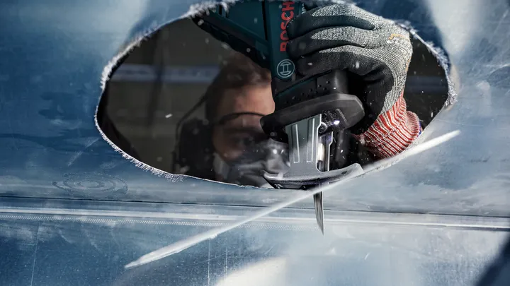 佩戴安全设备的人员用往复锯在金属上切出一个大洞。