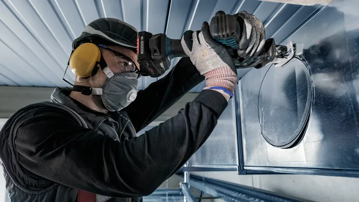 一名佩戴安全设备的人员使用电动工具在金属管道上切出一个圆孔。