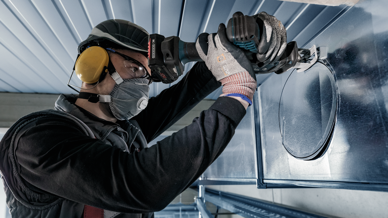一名佩戴安全设备的人员使用电动工具在金属管道上切出一个圆孔。