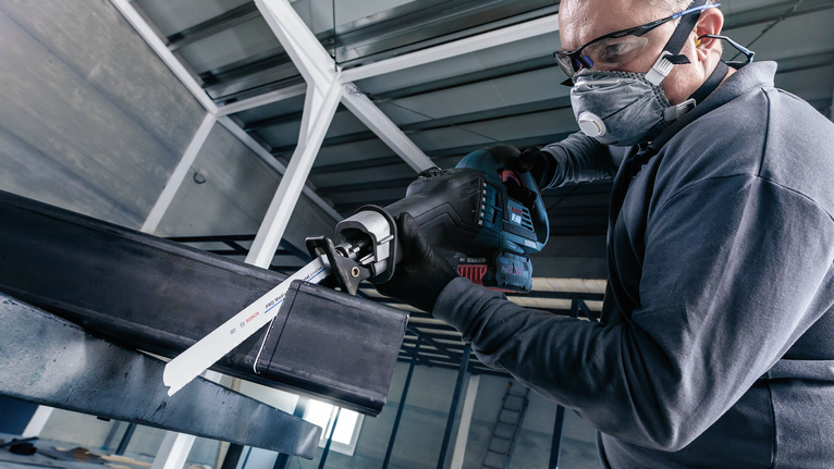 佩戴安全设备的人员使用往复锯切割钢梁。