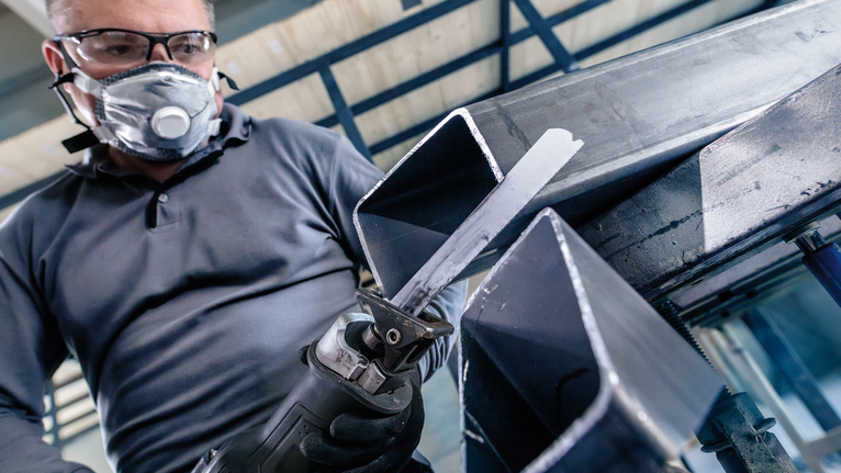 佩戴安全设备的人员使用往复锯切割金属梁。