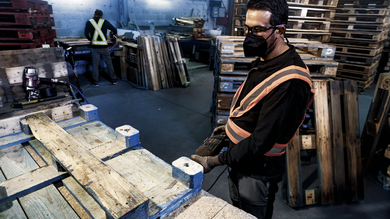 一名佩戴安全设备的人员使用电动工具在木质托盘上工作。