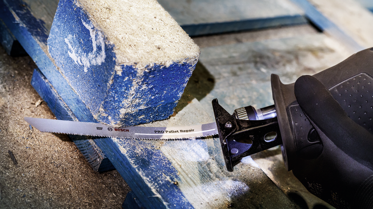 佩戴安全设备的人员使用往复锯切割木托盘。