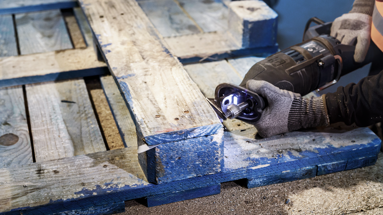 佩戴安全设备的人员使用往复锯切割木托盘。