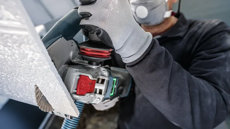 佩戴安全设备的人员使用电动工具切割面板。