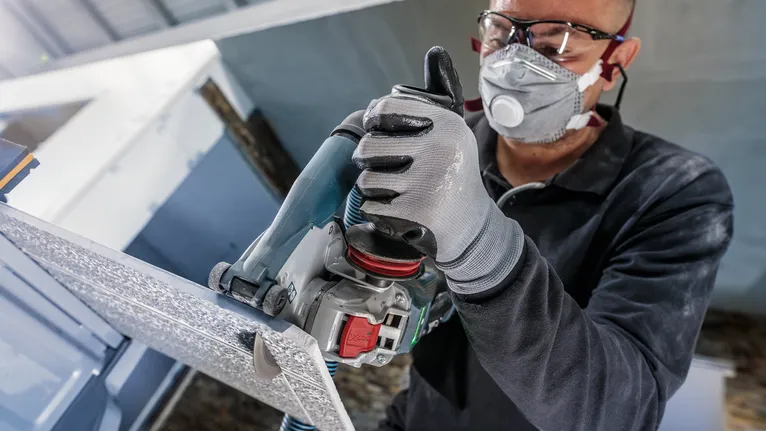 佩戴安全设备的人员使用电动工具切割金属板。