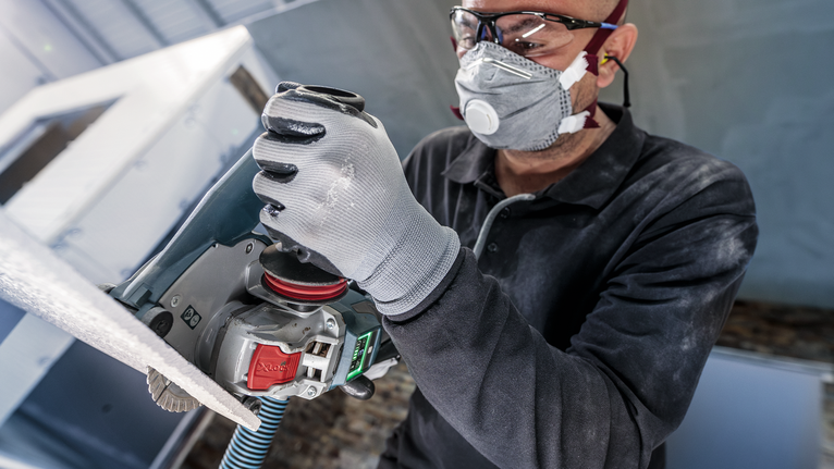 佩戴安全设备的人员使用电动工具打磨表面。